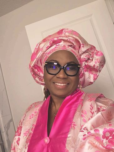 Woman wearing elegant pink traditional attire and glasses, smiling.
