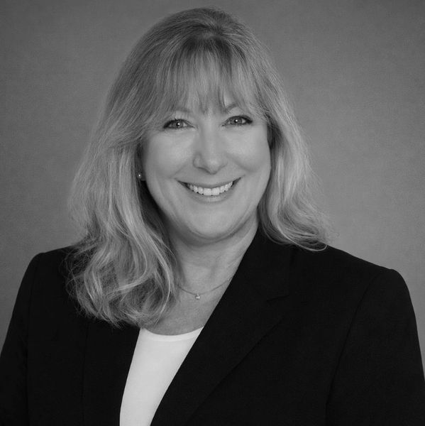 Professional black and white portrait of a smiling woman with blonde hair in a blazer.