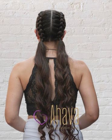 Woman with long wavy hair styled in two braids against a white brick wall.