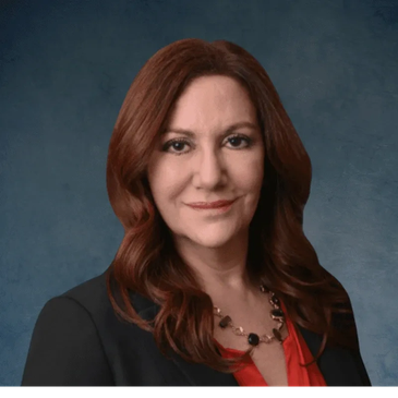 Professional woman with red hair wearing a black blazer and red blouse.