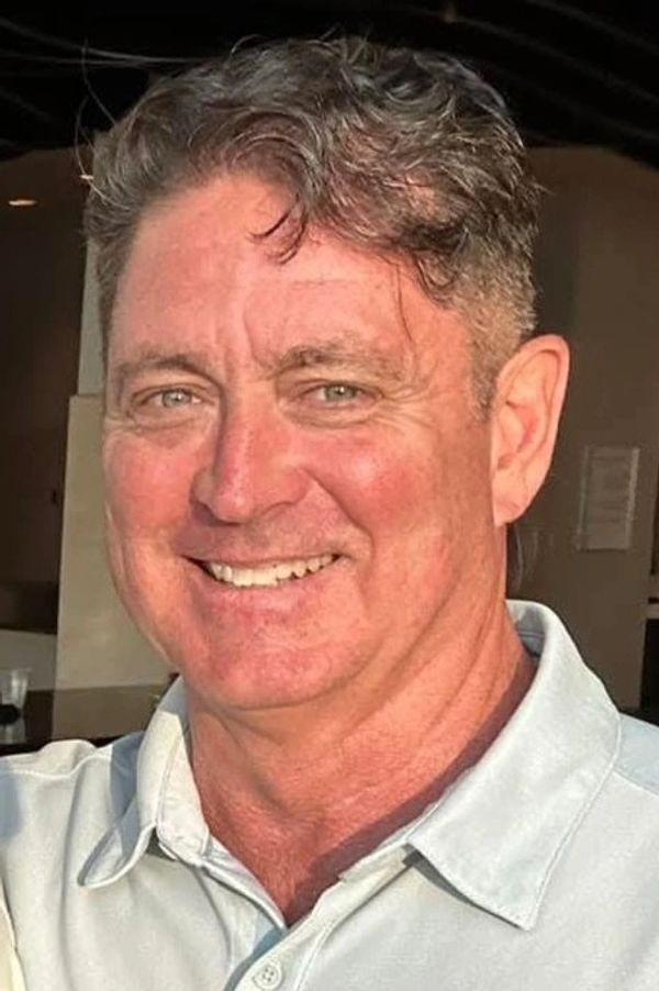 Smiling man with short wavy hair and a light-colored collared shirt.