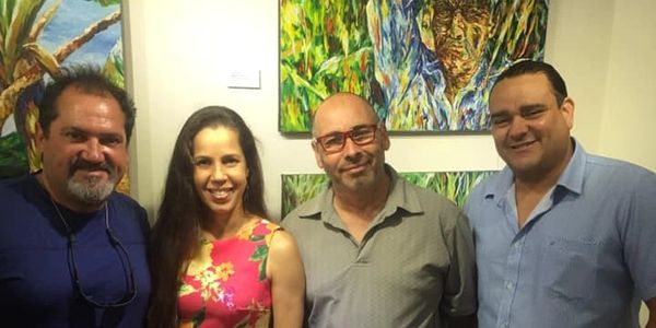 Four people posing smiling in front of colorful paintings.