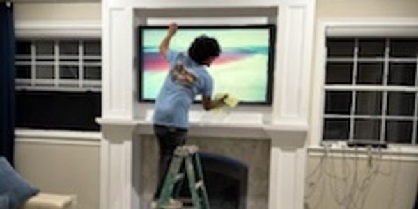 Person on ladder cleaning a TV screen in a living room.
