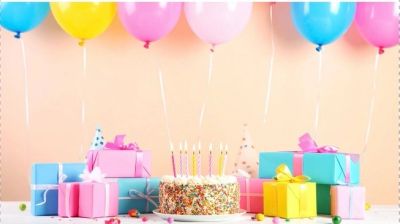 Colorful birthday setup with balloons, gifts, and a cake with lit candles.
