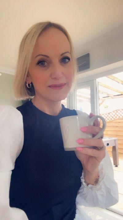 Woman with blonde hair holding a mug, smiling gently indoors.