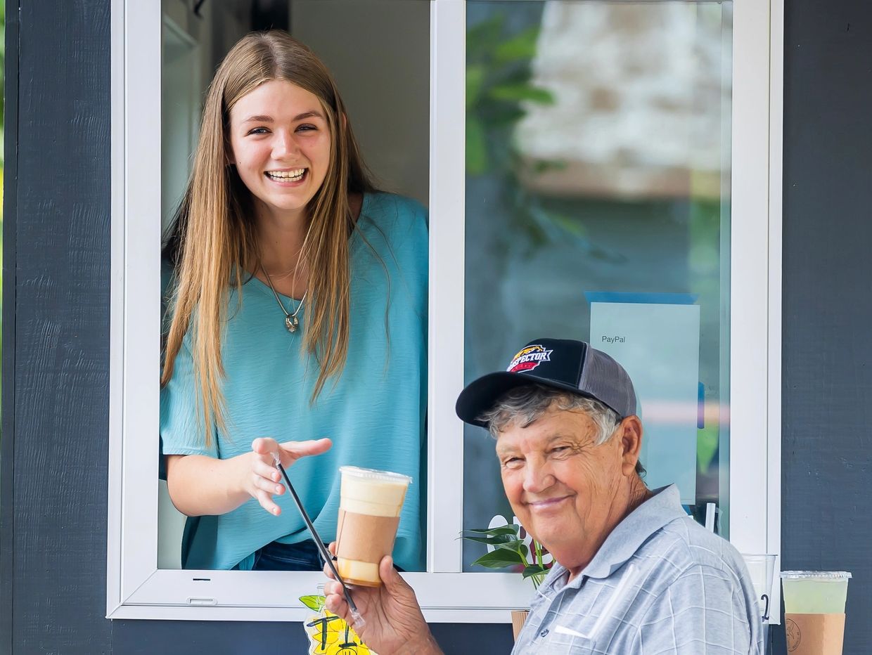 Happy young woman handing a drink to an elderly man at a service window.