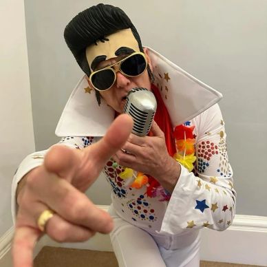 Person dressed as Elvis Presley singing into a vintage microphone.