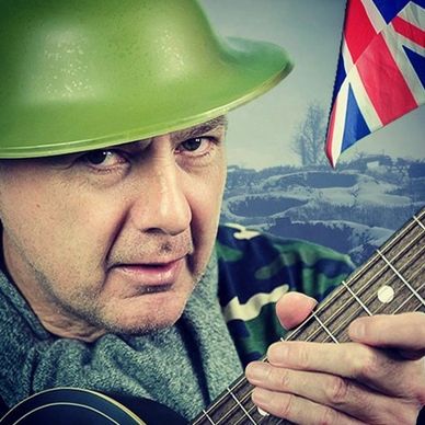 Man in green helmet playing guitar with British flag in background.