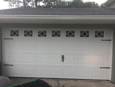 White double garage door with diamond-pattern windows and black decorative hinges and handles