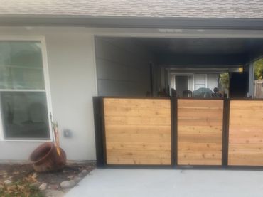 Wooden gate with horizontal boards and a black frame across a covered driveway