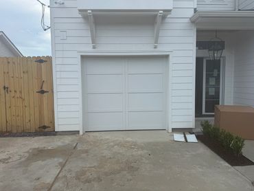 White single garage door on a white-sided home beside a wooden fence