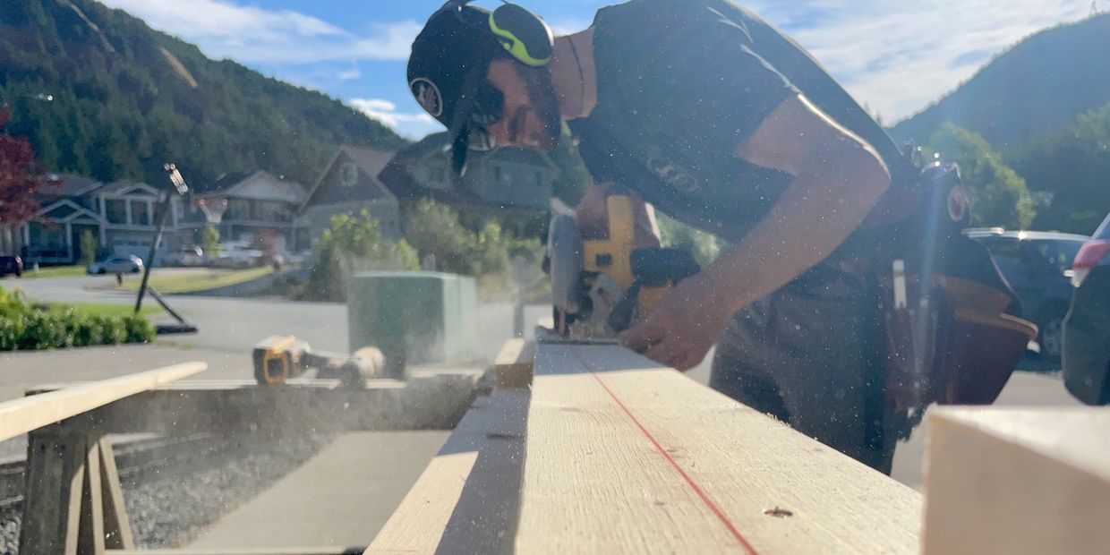Man using a power saw to cut wood outdoors on a sunny day.