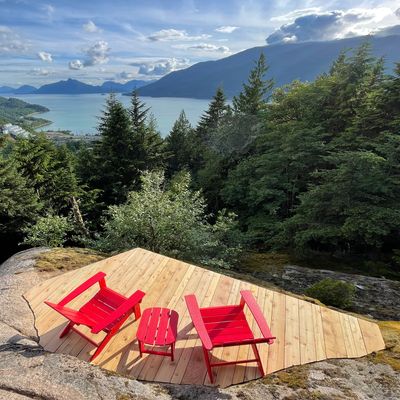 Two red chairs and a table on a wooden deck overlooking a lake and mountains.