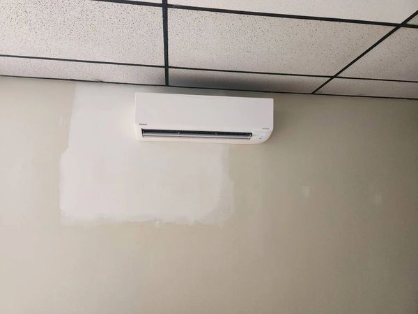 White air conditioner mounted on a beige wall with a partially painted white patch.