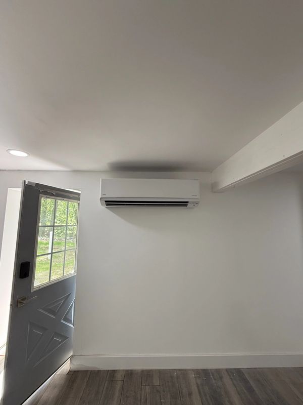 Modern air conditioner mounted on a plain white wall next to an open door.