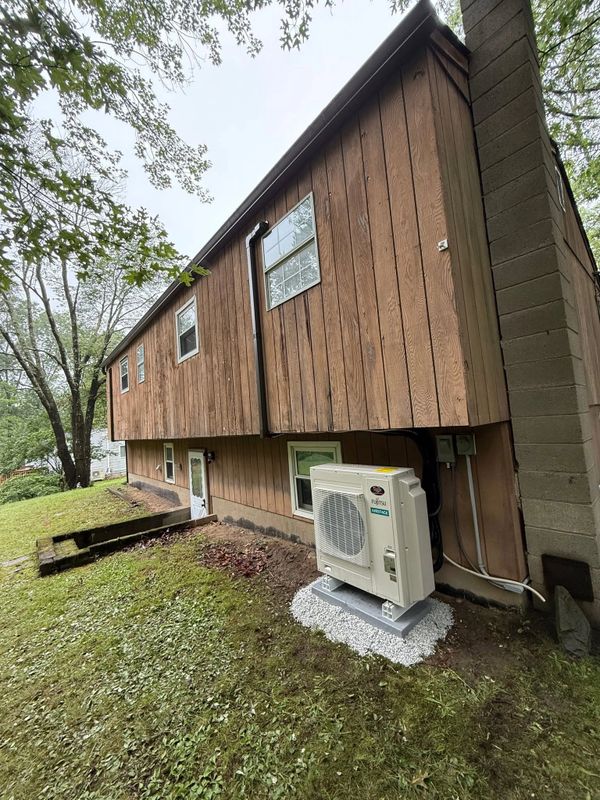 Outdoor Fujitsu air conditioning unit installed beside a wooden house.