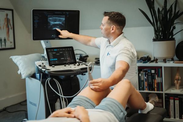A medical professional performing an ultrasound on a patient's knee in a clinic.
