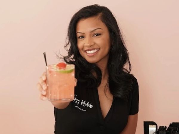 Smiling woman holding a refreshing cocktail towards the camera.