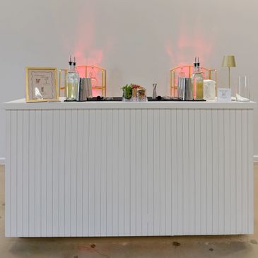 A modern white bar counter with bottles and decorative items.