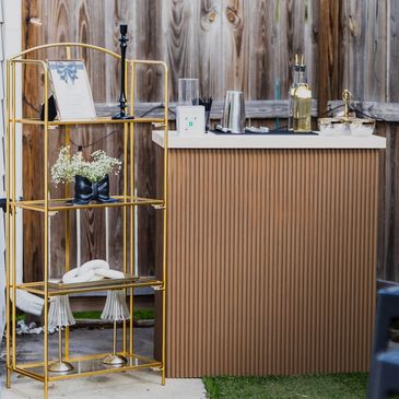 Elegant outdoor bar setup with gold shelving and wooden backdrop.