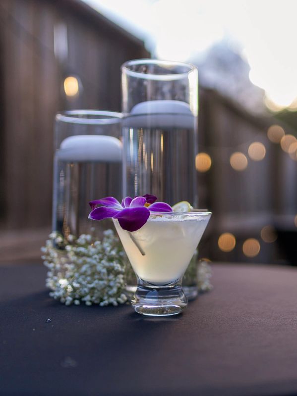 Elegant cocktail with a purple flower garnish and tall candles in the background.