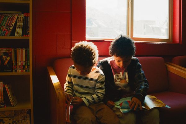 Two children reading books together on a couch in a cozy room with natural light.