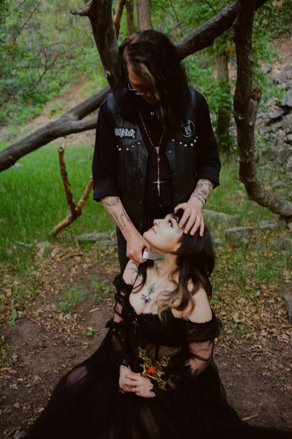 A man holds a knife to a woman's throat in a dark, dramatic forest scene.