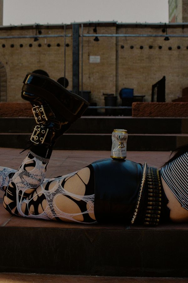 Person lying down wearing edgy, torn leggings and black boots with a beer can on their hip.