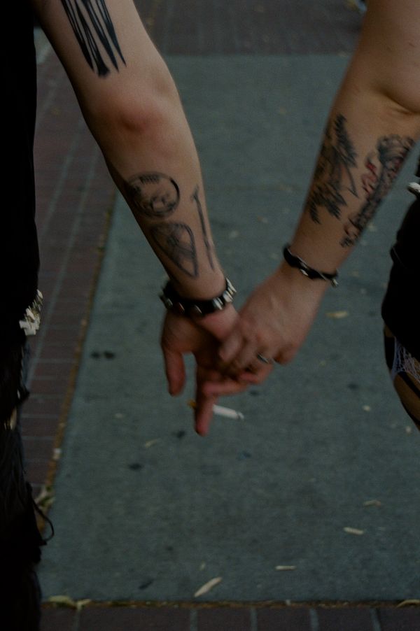 Two tattooed arms holding hands, one with a cigarette.