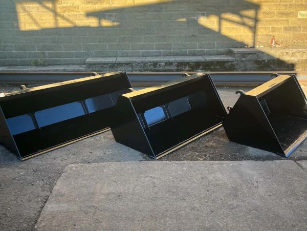 Three large black metal buckets in a row on concrete.