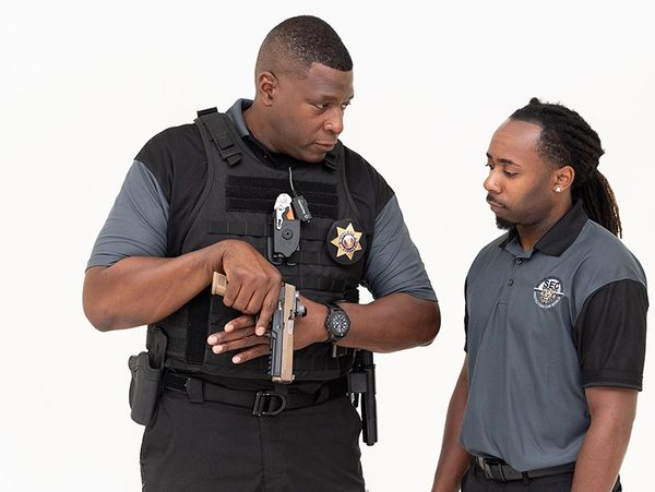 Security officer holding a gun talks to a man in a gray and black shirt.