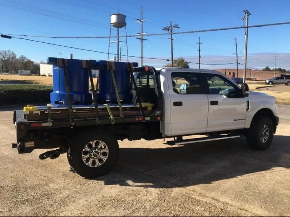 Truck with two large cylinders strapped down to the trailer bed.