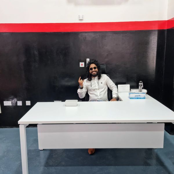 Man in white shirt sitting at a modern white desk, smiling and gesturing.
