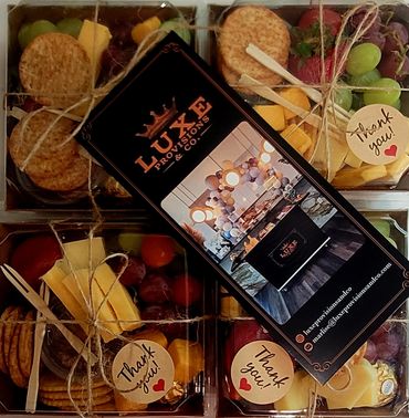 Elegant gift boxes with cheese, crackers, grapes, and thank you tags.