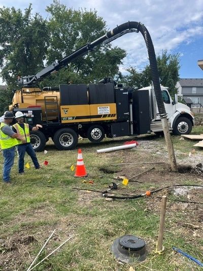 Construction workers operating a vacuum excavation truck at a site.