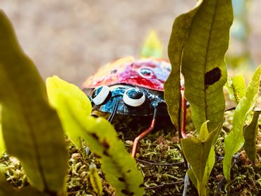 A colorful ladybug figurine peeking through green leaves on moss.