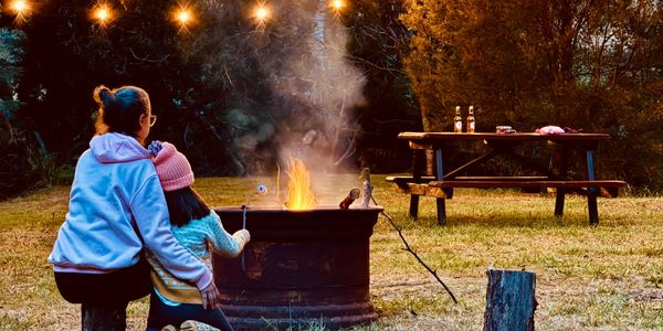 Two people roasting marshmallows by a campfire under string lights.
