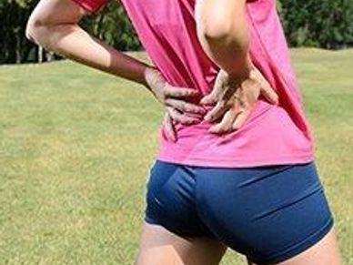 Person holding their lower back outdoors, possibly in pain.
