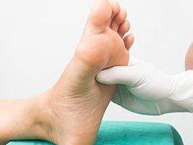 Gloved hand examining a person's foot sole in a clinical setting.
