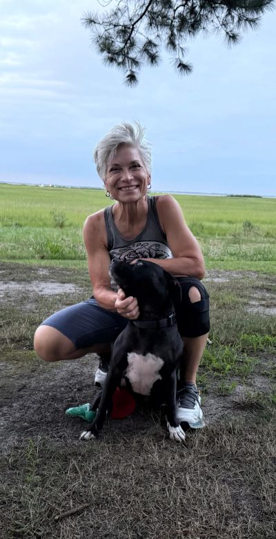 A woman smiling and crouching with her black dog outdoors.