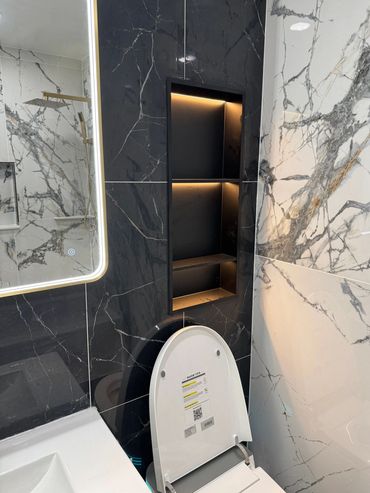 Modern bathroom with black and white marble walls and illuminated shelves.