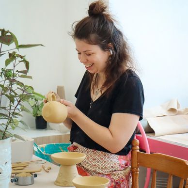 A woman happily crafting pottery in a bright studio.