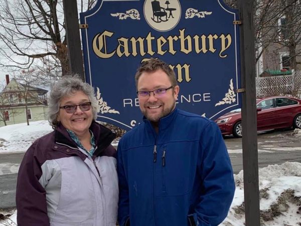 Two people smiling in front of a Canterbury Inn Residence sign.