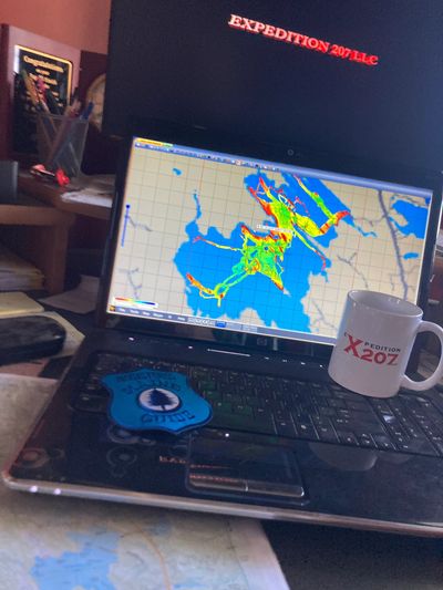 Laptop displaying a colorful map with a mug and Maine guide patch nearby.