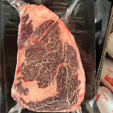 Vacuum-sealed marbled beef steak on a black tray.