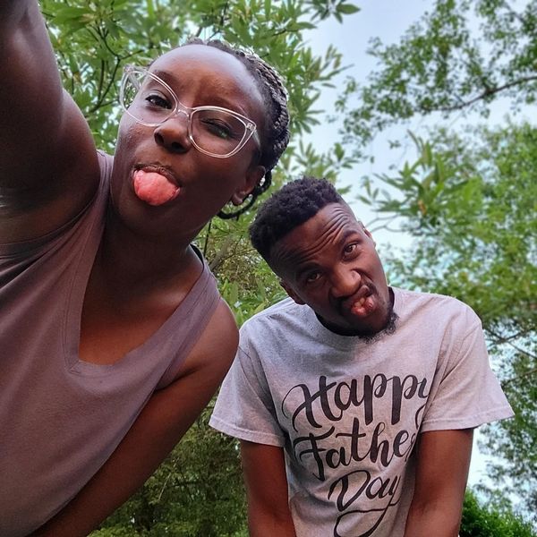 Two people making funny faces outdoors, one wearing a "Happy Father's Day" shirt.