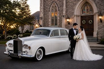 Newlyweds pose beside a classic white Rolls-Royce Silver Cloud III