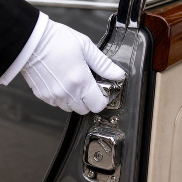 Gloved hand opening a classic car door with polished chrome details.