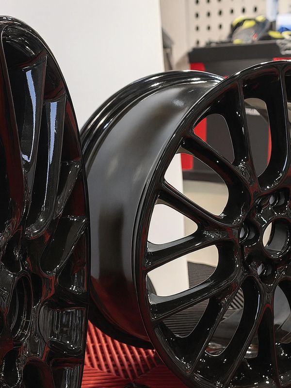Glossy black multi-spoke car rims displayed indoors.