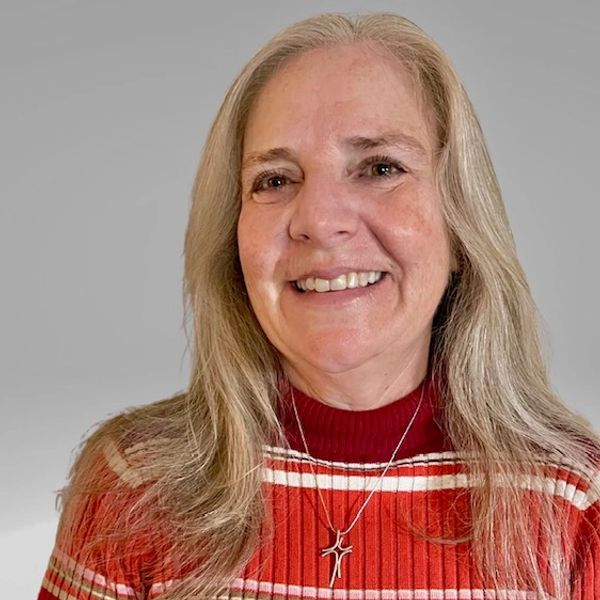 Smiling woman with long blonde hair wearing a red striped sweater and cross necklace.